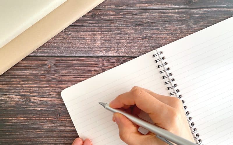 Writing,Notes,In,Notebook,On,Wooden,Desk,With,Pen